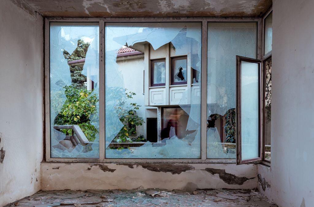 Damaged room overlooking buildings through a broken window