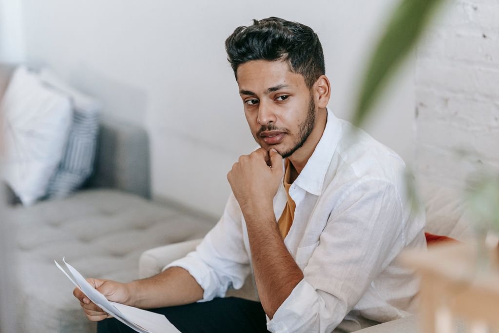 Should I Invest or Pay Off Debt First? A Practical Decision Guide Man holding paperwork while seated on a sofa