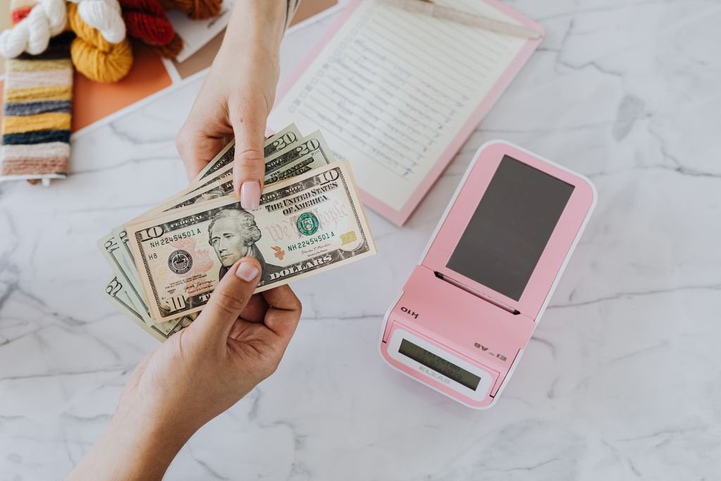 Gross Pay vs. Net Pay: Differences and How to Calculate Each Hands counting dollar bills beside a phone and paperwork