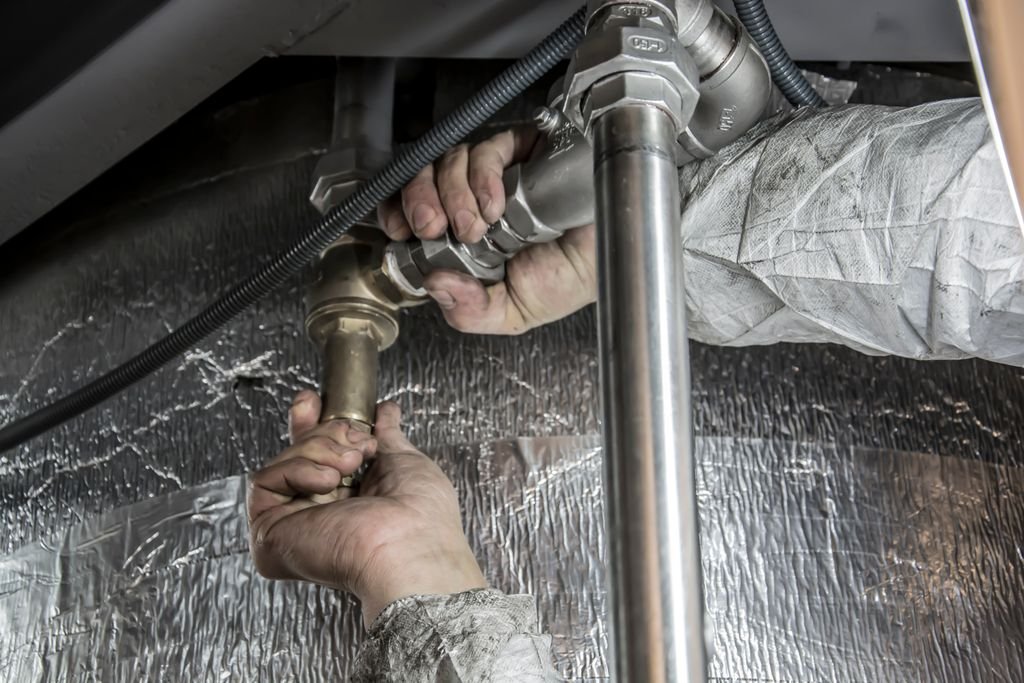 Hands repairing metal plumbing pipes under a sink