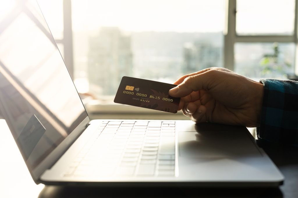 ACH vs EFT: What’s the Difference and Which Should You Use? Person holding a payment card beside a laptop
