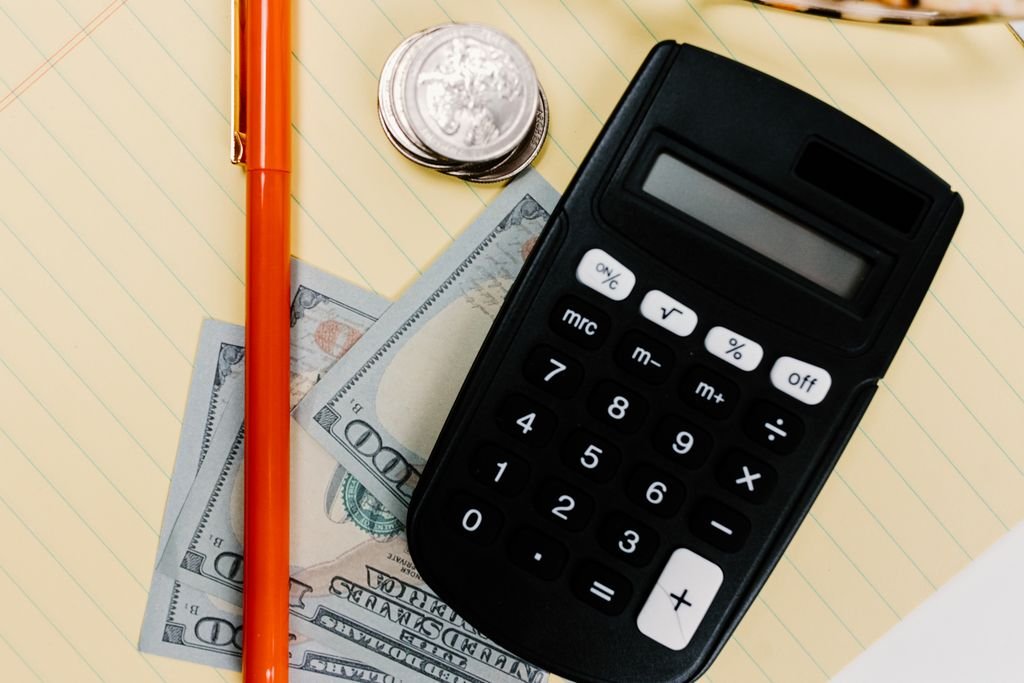 Market Value Adjustment: How It Affects Annuity Withdrawals Black calculator, red pen, coins and dollar bills on a yellow notepad