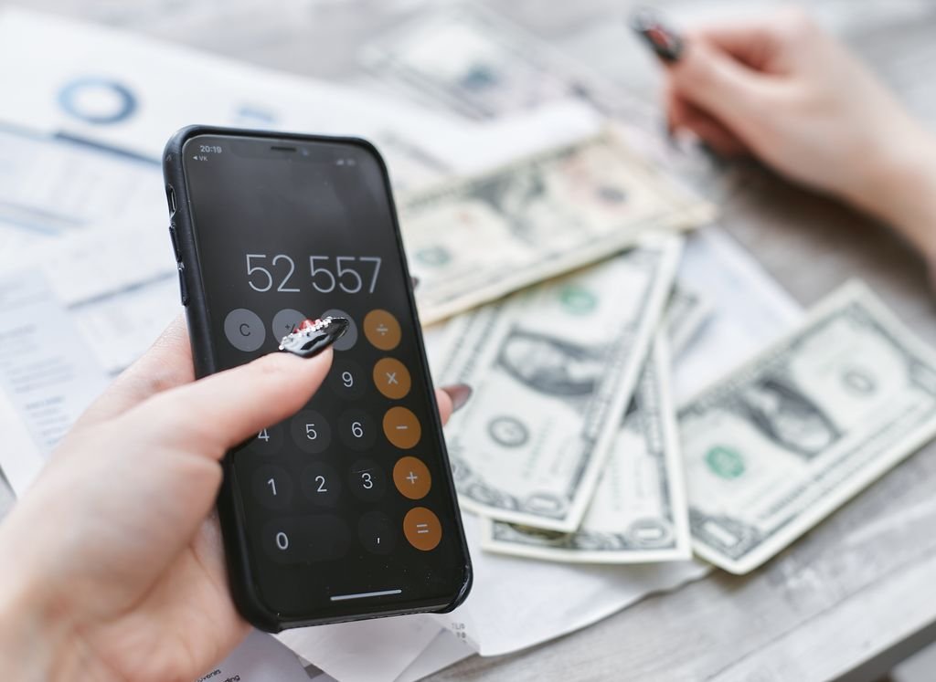 Hands using a smartphone calculator beside dollar bills for budget planning
