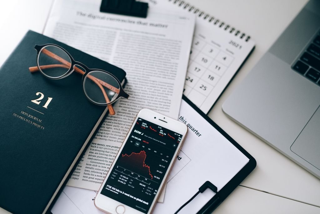 Buy Borrow Die Strategy: How It Works and Its Risks Smartphone displaying stock data beside financial documents, eyeglasses and a laptop
